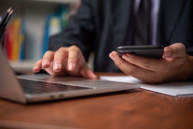 Profissional utilizando laptop e dispositivo móvel para analisar dados patrimoniais na Protekto